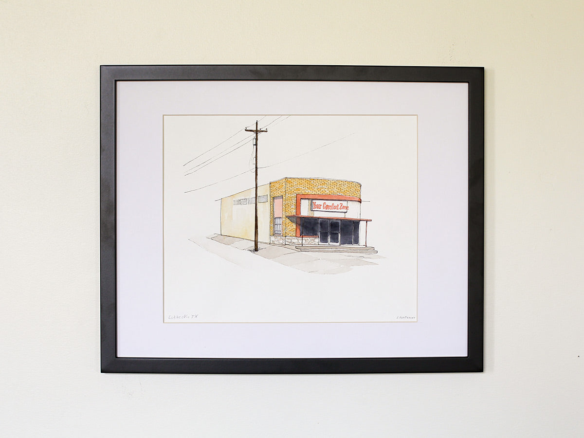 Framed original watercolor art on white wall with black wood frame.
