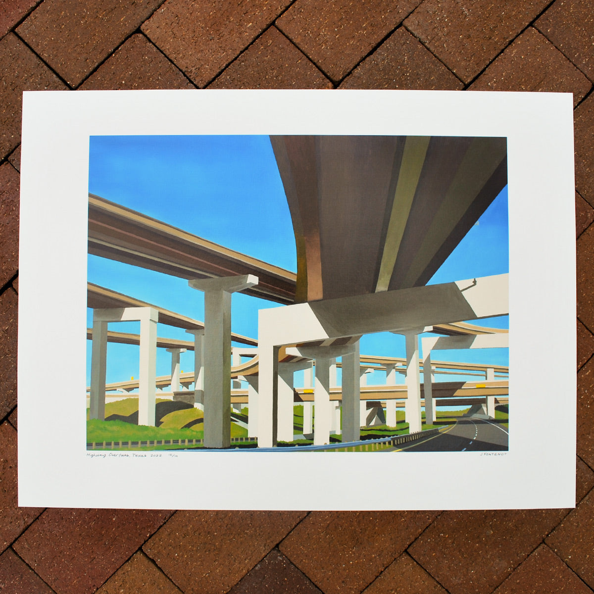 Art print against brick background, oil painting of Texas highway interchange image in the center with a white margin all around.