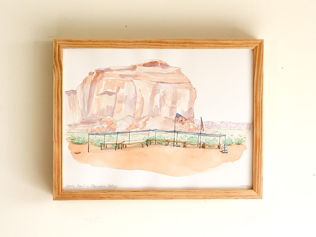 Framed original watercolor art on a white wall. Frame is warm natural wood. 