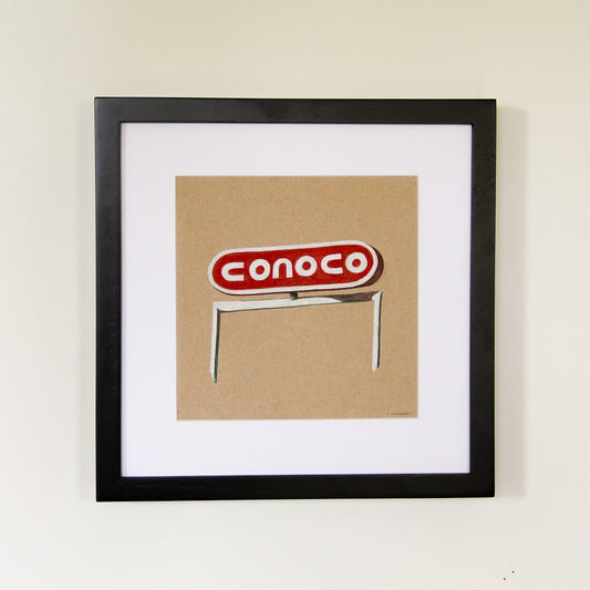 Framed artwork hung on white wall. Colored pencil drawing on tan toned paper of a red and white Conoco gas road sign with a 2 inch white matte around the art in a black wood frame. 